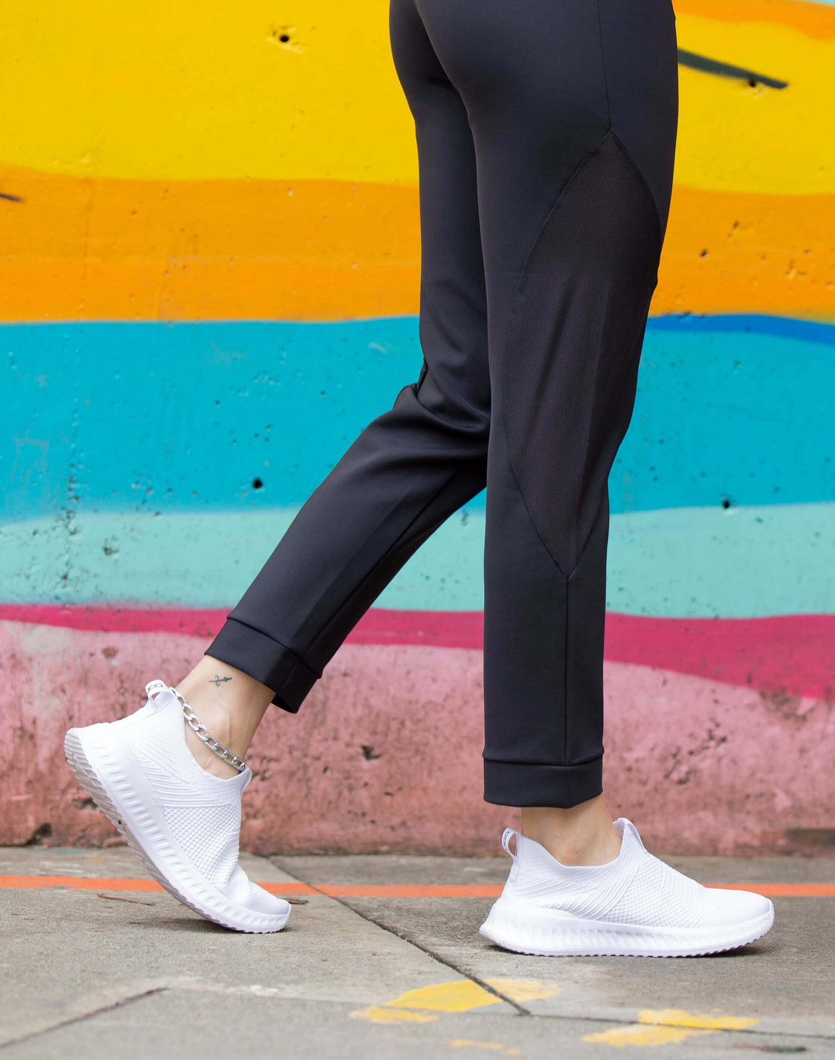 Person wearing white sneakers and black athletic pants against a vibrant graffiti background.