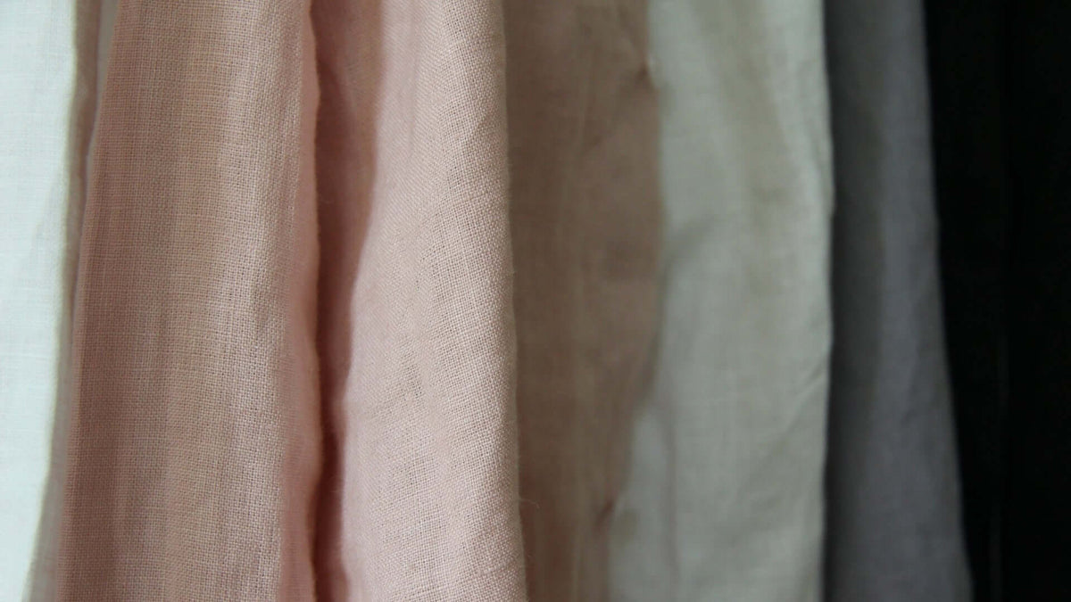 Close-up of hanging textured linen fabrics in soft pastel and neutral colors.