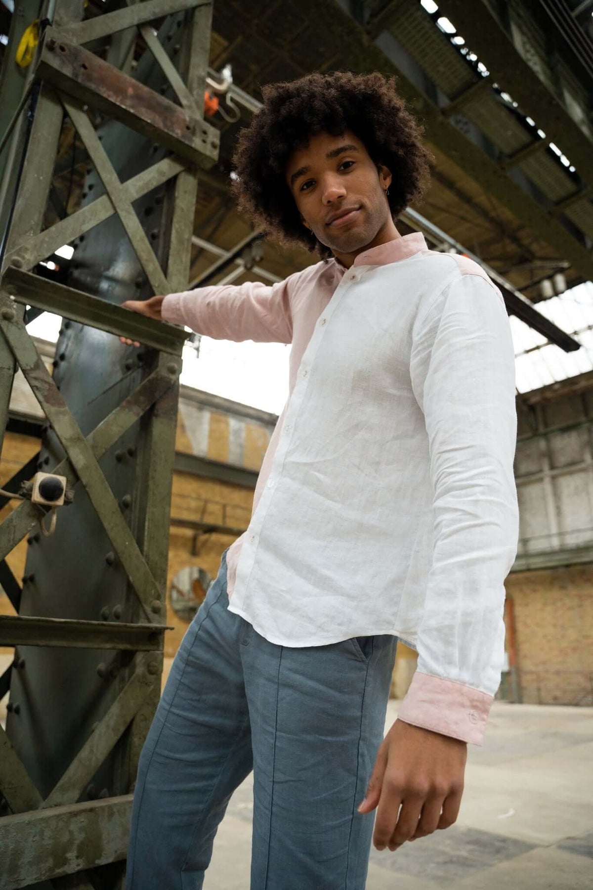 Man with curly hair in a two-tone shirt posing against an industrial backdrop.