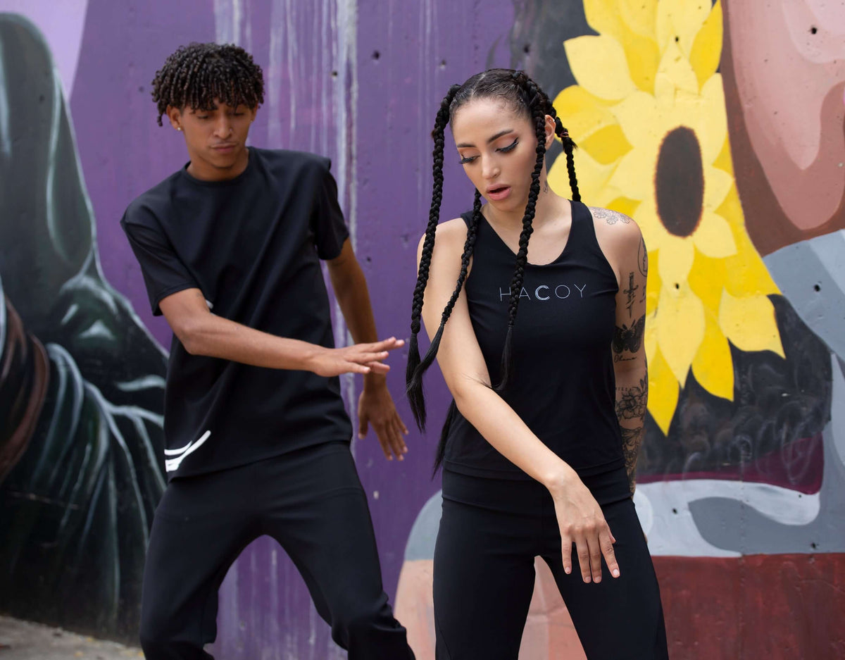Two dancers in urban attire perform in front of a vibrant mural, showcasing style and movement.