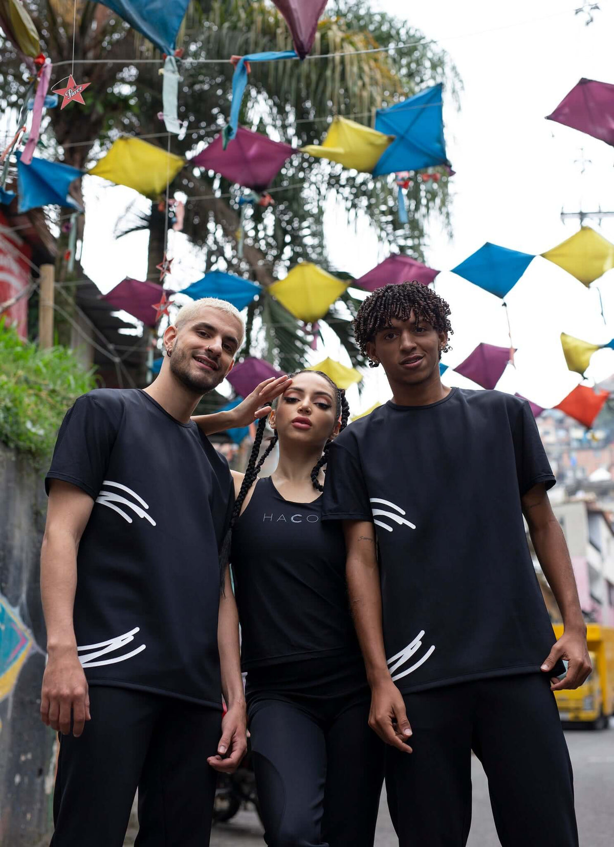 Three models wearing HACOY streetwear in an urban setting adorned with colorful kites.