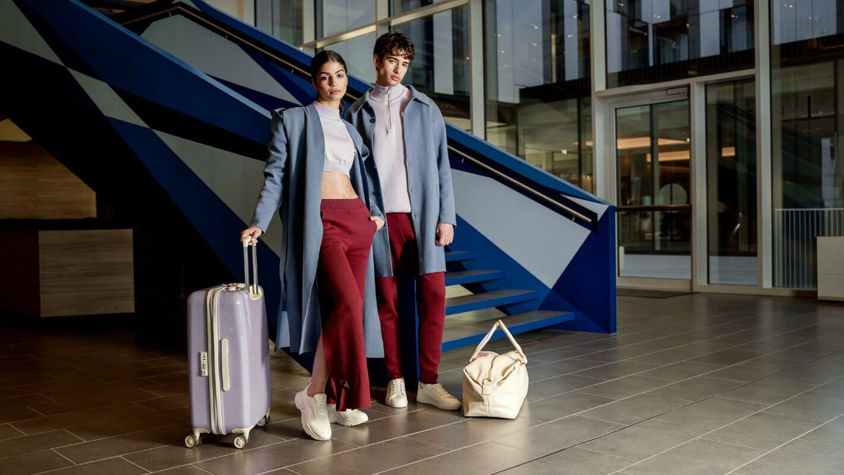 Fashionable couple in stylish outfits with luggage at a modern staircase, showcasing travel elegance.