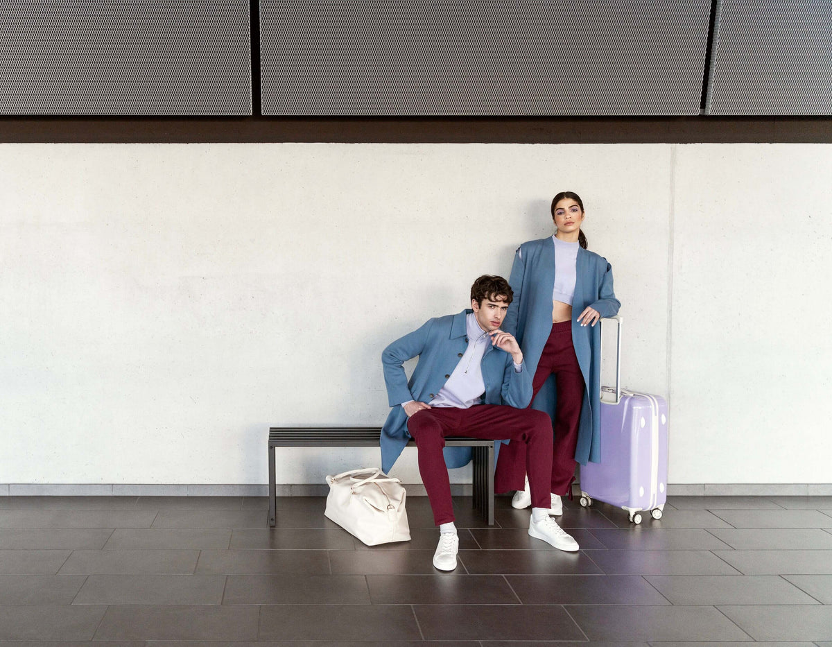 Fashionable couple at an airport; stylish outfits with a suitcase and travel bag, modern travel aesthetic.