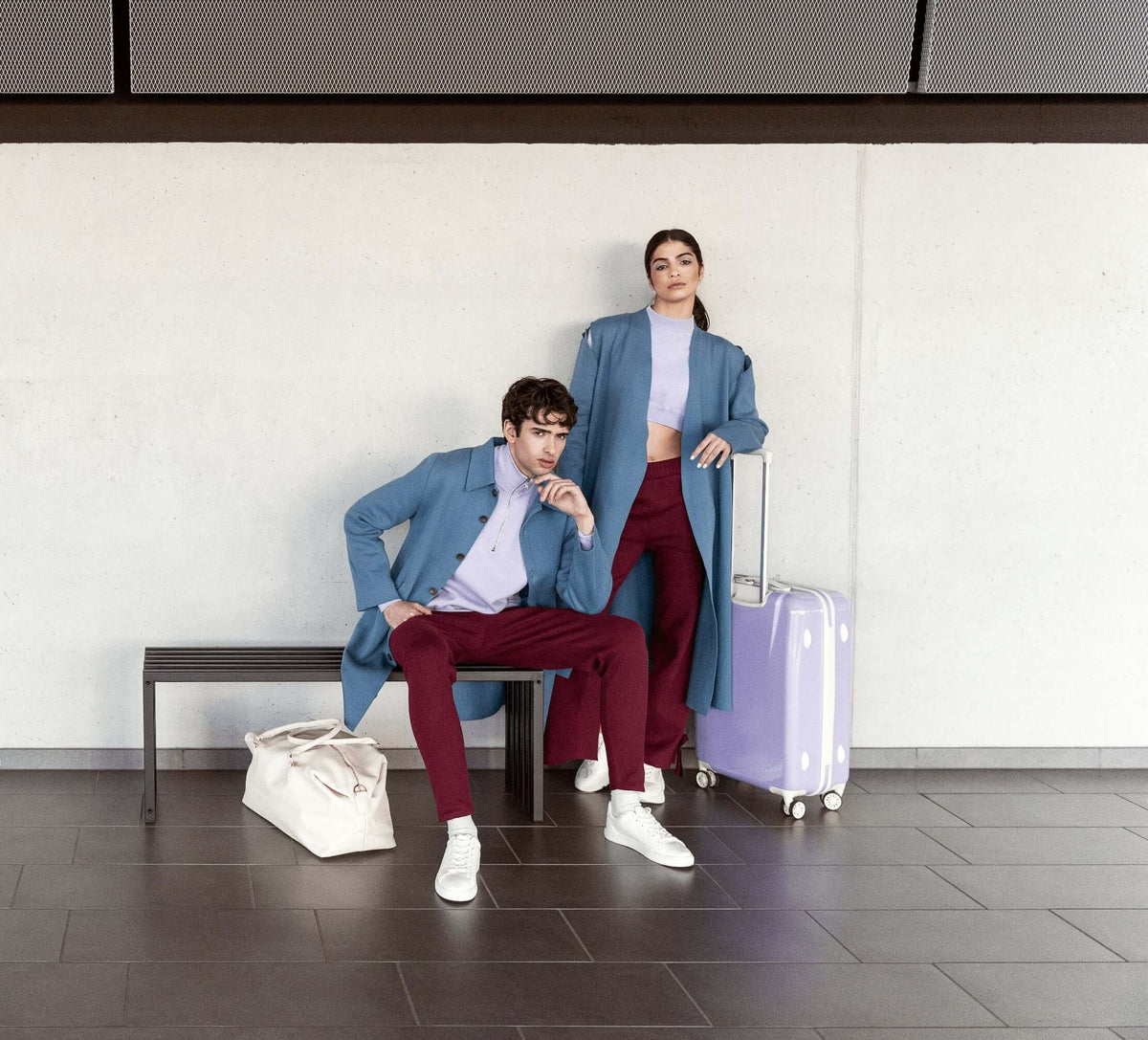Fashionable young couple posing in modern attire with suitcase and bags, showcasing contemporary travel style.
