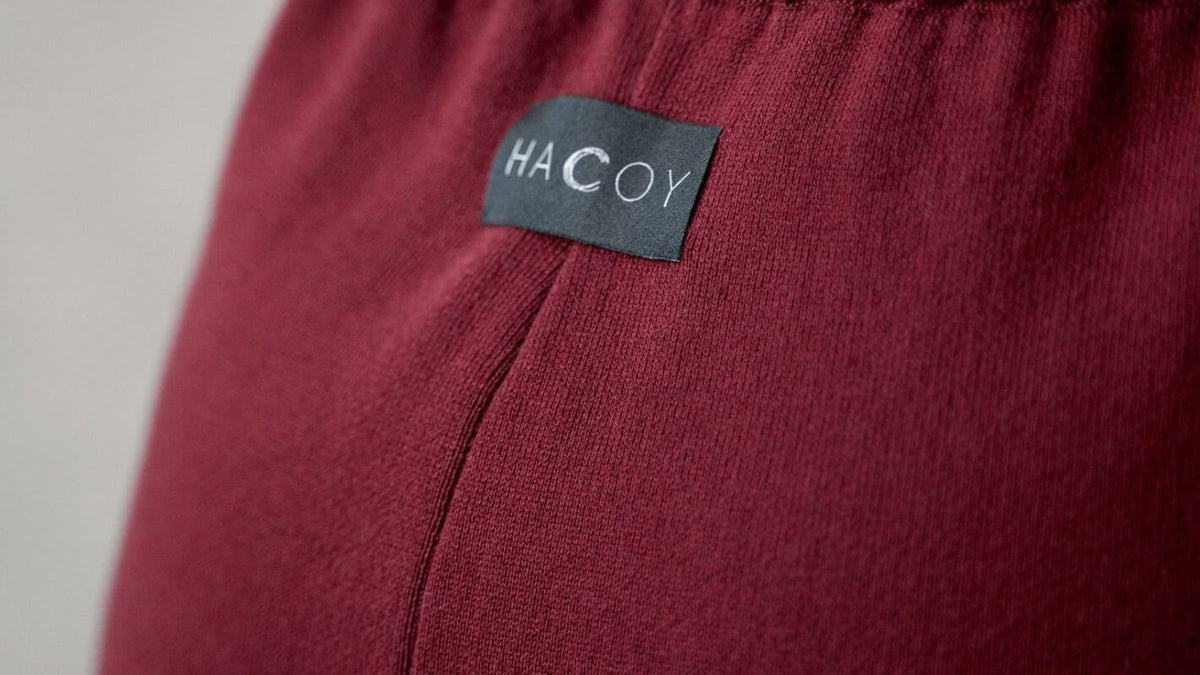 Close-up of HA C OY logo on burgundy fabric, showcasing quality and understated elegance.