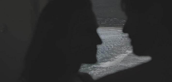 Silhouettes of a couple against a coastal backdrop, capturing an intimate moment by the water.